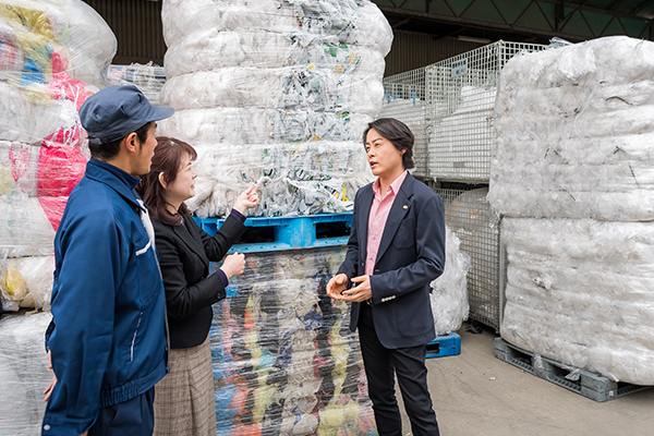 背後に積まれた「資源」である廃プラについて説明を受ける河村さん